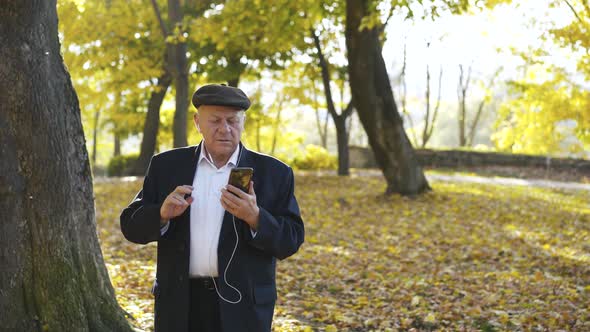 Senior Man Having Fun When Talking on Phone Camera Through Headphones Outside alt