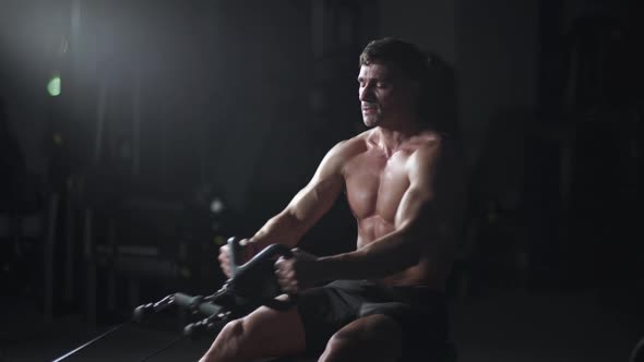 Athletic Man in the Gym Lifting Blocks on Rowing Machine Training on Block Device and Gym Equipment alt