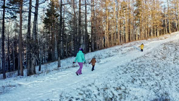 A Mother and Two Sons are Running Along a Path in a Winter Forest