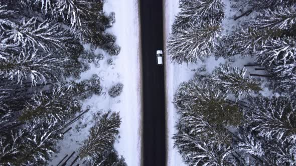 Aerial top view snowy forest mountains with cars driving winter road.