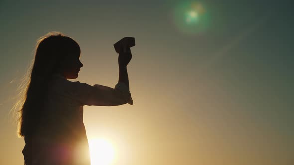 Profile of a Girl Playing with a Paper Airplane at Sunset alt