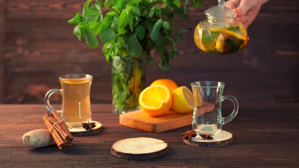 Pouring Tea With Lemon, Orange, Ginger And Mint In Cup On Rustic Wooden Table In The Morning