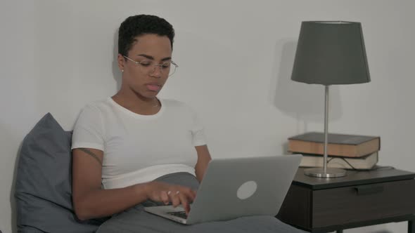 African Woman Showing Thumbs Down Sign While Using Laptop in Bed alt