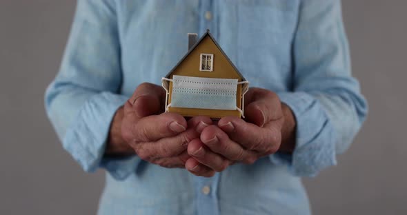 Businessman holding model of house with medical mask in hands
