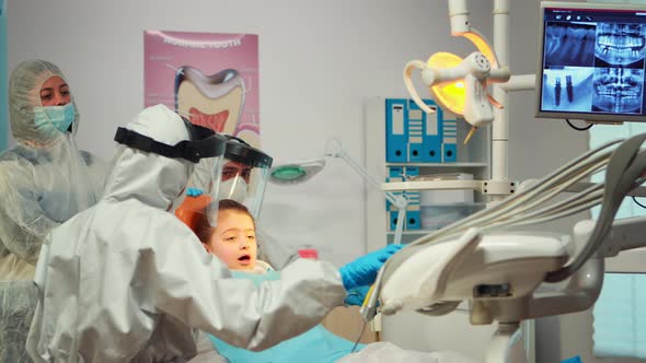 Little Girl Wearing Ppe Suit Looking in the Mirror After Dental Intervention alt