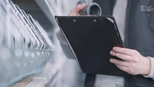 Male Hand Holding List of Products Checking Pipe Connector and Writing Register alt