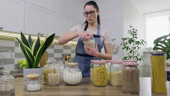 Storing Food in Kitchen Woman Housewife in an Apron with Jars and Containers alt