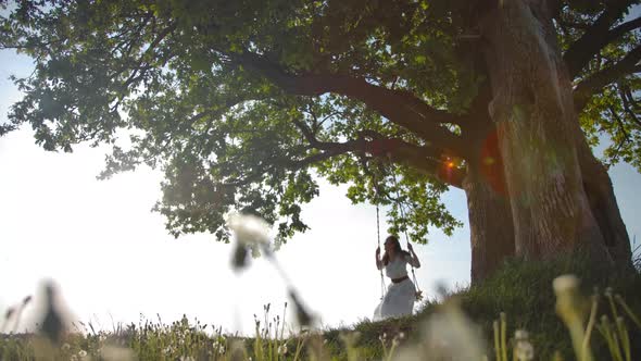 Wide View of a Young Girl Swinging. She Is Carefree and Happy in Flying Over a Green Field. alt