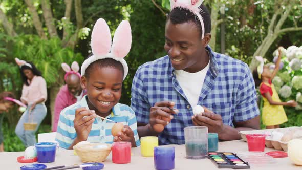 Animation of happy african american father and son painting easter eggs in garden alt