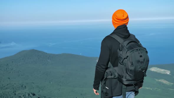 Male Hipster Tourist in Hat Putting on Sunglasses Enjoying Great Blue Sea and Sky alt