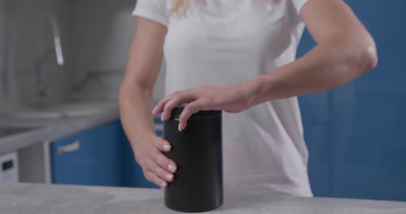 Female Hand Grabs Black Jar and Unscrews Lid on It