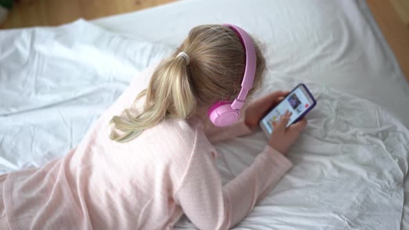 Modern Life of Generation Z. Teenage Girl in Pajamas and Headphones in the Room on the Bed Listens