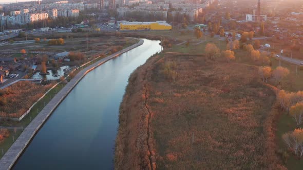 River in the city overgrown with reeds, autumn trees on the shore alt