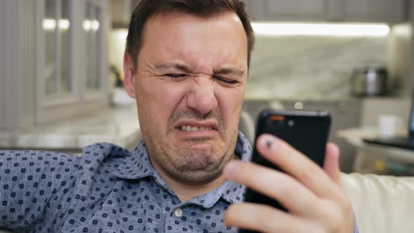 Annoyed Millennial Man with Disgust Look at Smartphone Screen at Modern Living Room alt