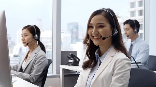 Woman wearing microphone headset working in customer service support help desk with colleagues