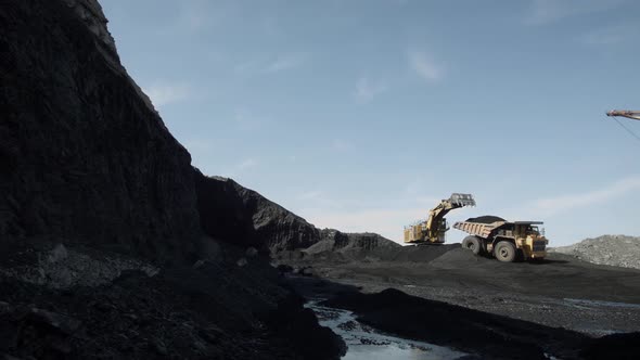 Open Deep Coal Pit with Heavy Machinery in Operation Against Bright Blue Sky