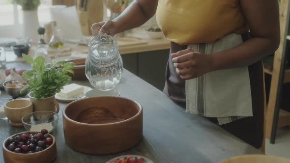 African American Woman Adding Water to Bowl while Cooking alt