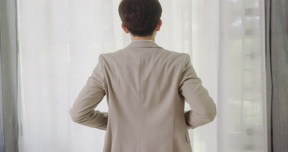 Handsome Man Puts Suit On During Morning Wedding Day. Young Groom Standing In Front Of The Window. alt