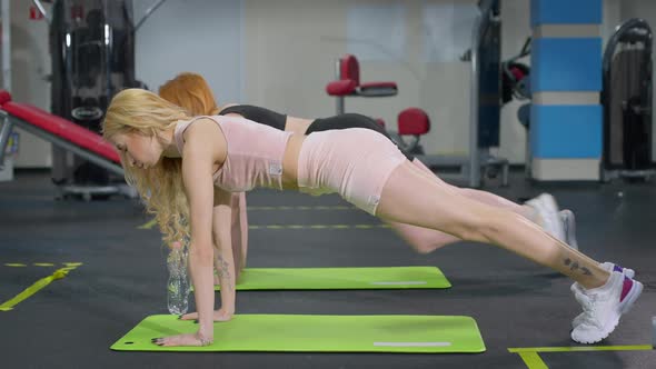 Side View of Slim Fit Caucasian Sportswomen Standing in Plank Position in Gym on Exercise Mat alt