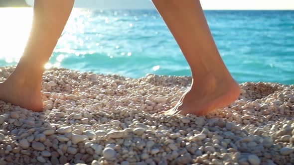 Closeup woman's legs walking on a beach at sunset over a sea.