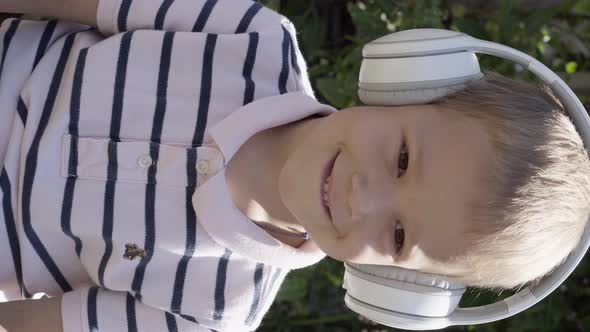 Vertical Shot Portrait of Cute Little Boy With White Headphones Listening to Music