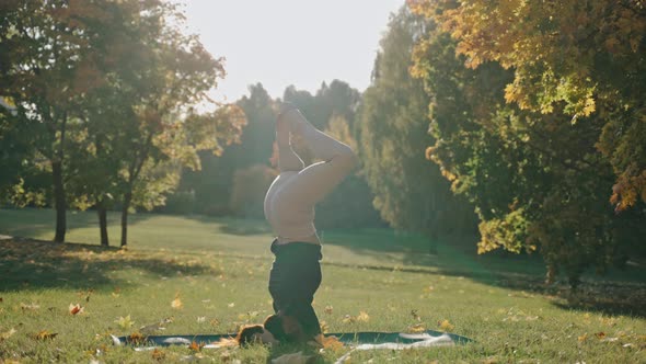 Young Woman Practicing Headstand Yoga Pose in City Park on Sunny Autumn Day