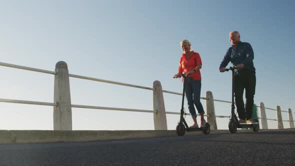 Senior couple using electronic scooters alongside beach alt