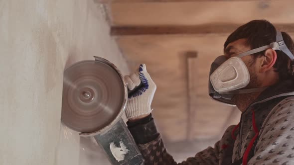 Caucasian Male Worker Wearing Respirator Using Angle Grinder to Cut Wall in Slowmotion alt
