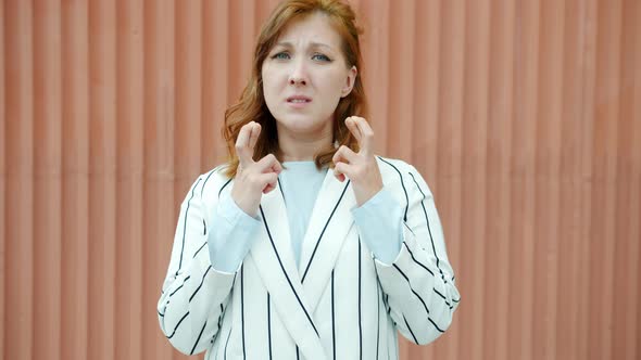Slow Motion Portrait of Hopeful Redhead Lady Crossing Fingers and Making Wish Outdoors alt