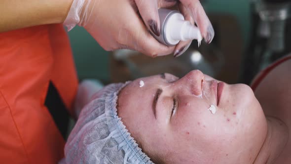 Beautician Applies Moisturizer Onto Large Woman Face Closeup alt