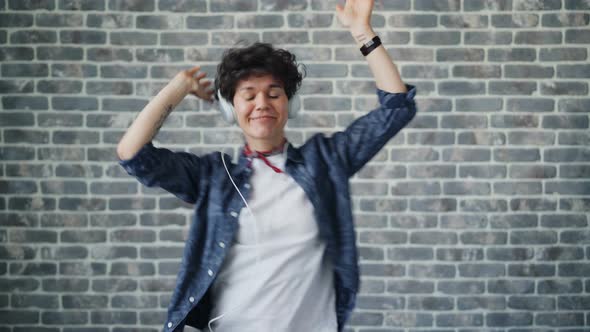 Portrait of Cute Hipster Dancing in Headphones on Brick Background Having Fun alt