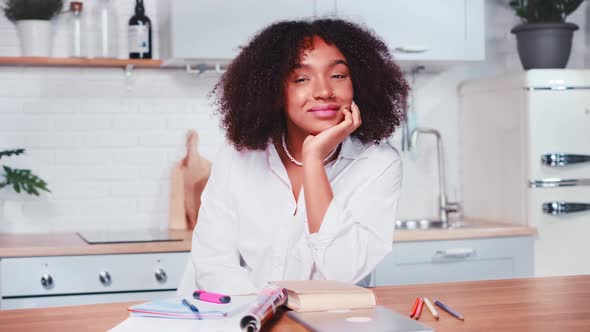 Young African American Woman Smiles Sits at Kitchen Table of Own House alt