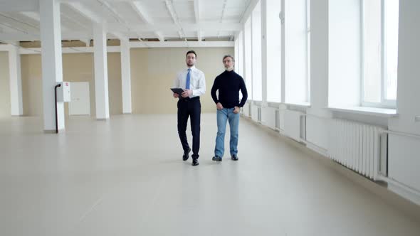 Realtor shows client an office space for rent, front view. Realtor and client walk around alt