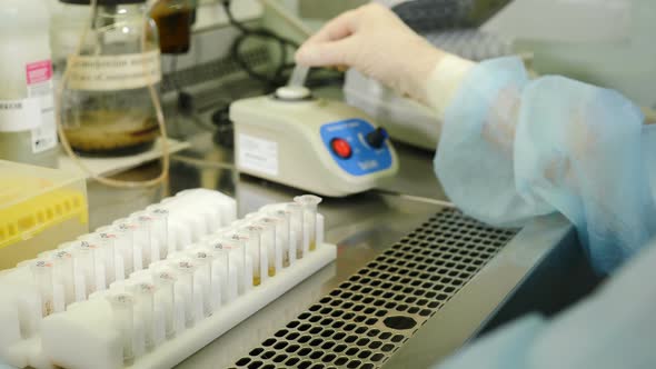 Scientist Working in Sterile Genetics Laboratory with Pipette in Medical Dressing Gown alt