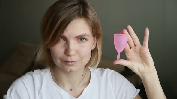 Young Woman is Showing Menstrual Cup and Laughing While Sitting at Home Room Iroi alt