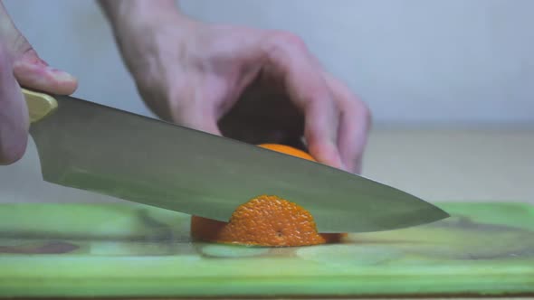 A Man's Hand Cuts Half an Orange on the Table with a Knife