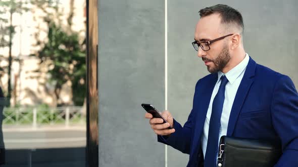 Trendy Businessman in Suit and Tie Use Smartphone Going Near Modern Building alt