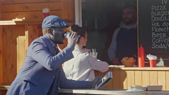 Serious African American man drinking coffee near food booth