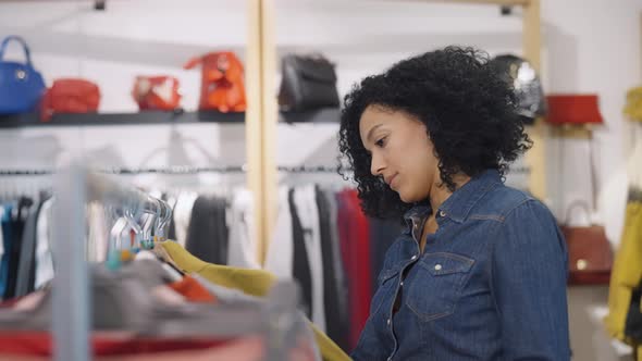 Female Customer Makes Purchases in Clothing Store Chooses Stylish Clothes Hanging on Rack Hangers alt