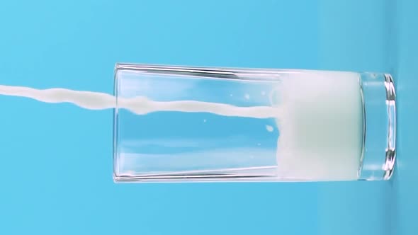 Vertical Video Slow Motion Closeup Shot of Milk Cold Beverage Drink Pooring Into Low Glass Blue