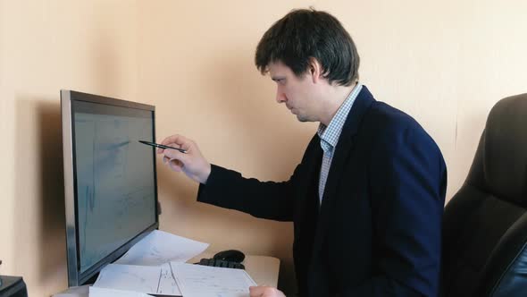 Man Works at a Computer. Compares Graphics on the Screen and on Paper.