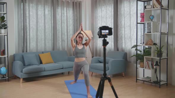 Asian Trainer Female In Sports Clothes Speaking To Camera And Doing Yoga In High Lunge Pose alt
