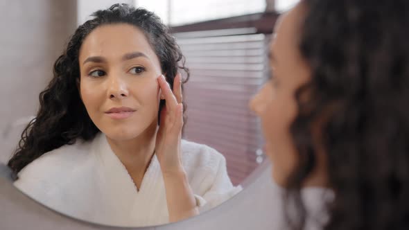 Young Attractive Woman in Bathrobe Looks in Mirror in Bathroom Touches Moisturized Face After alt