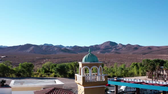 Drone circles around a tower in a small town in the middle of desert. Birds flying by alt