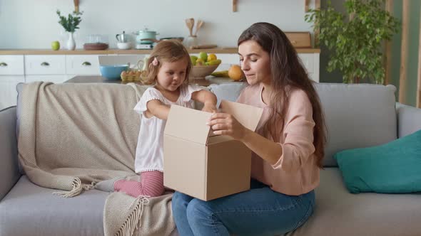 Adorable Girl Unpacking the Order. Happy Mother and Daughter Unpacking the Order. alt