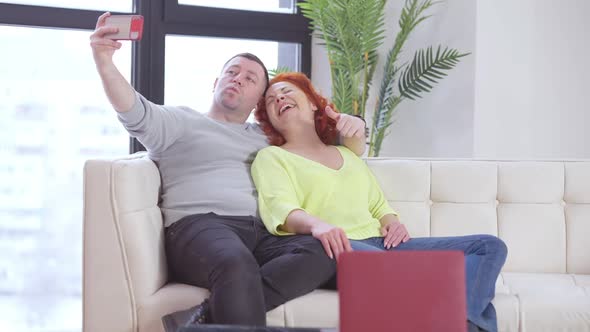Cheerful Carefree Man and Woman Taking Selfie Sitting on Couch in Living Room alt