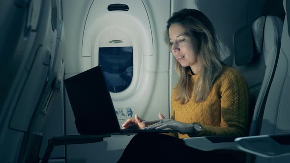 Aircraft Cabin at Night with a Lady Smiling While Typing on a Laptop. Female Freelancer Working on alt