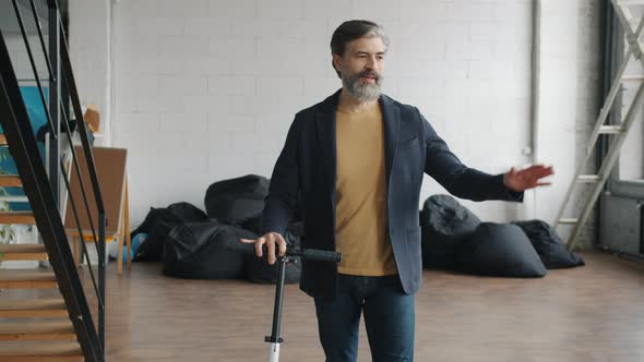 Mature Man Arriving To Office with Scooter Saying Hi Waving Hand Smiling Walking alt
