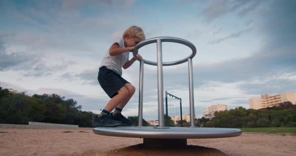 Happy Child on Playground Spinning on Carousel Swing and Laughing on Sunset