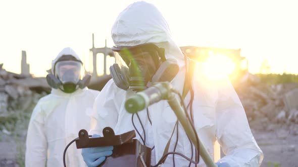 Portrait of Two Scientists in White Overalls and Protective Masks Taking Measurements of Radiation alt